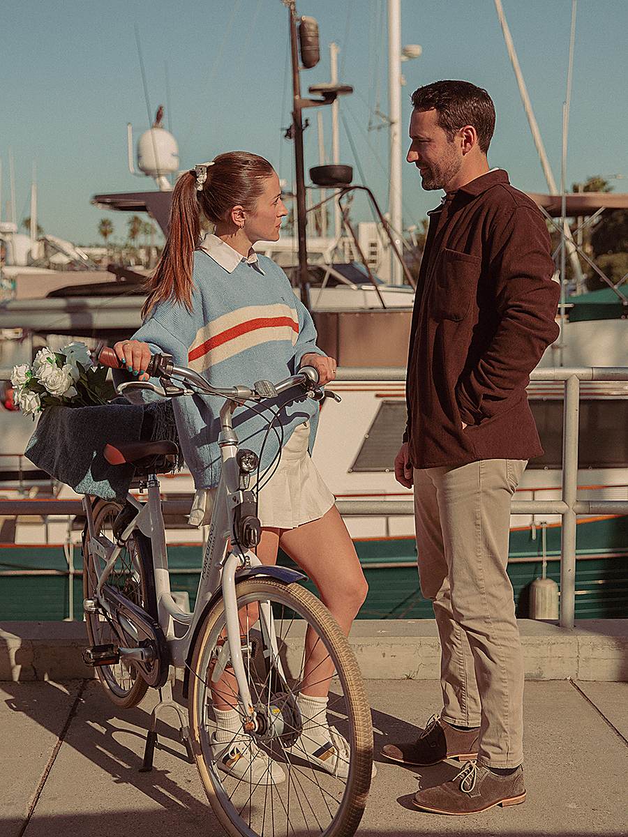 Couple with a beach cruiser bike exploring the waterfront boardwalk at The Portofino Hotel & Marina in Redondo Beach, California.
