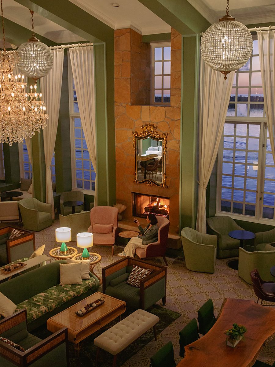 Elegant fireside lobby lounge at The Portofino Hotel & Marina in Redondo Beach, California, with crystal chandeliers, sage green seating, and tall windows overlooking King Harbor at sunset.